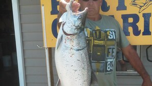 A man holding a large fish in front of a sign with partially visible text.