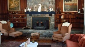 A cozy living room with a stone fireplace, two armchairs, a coffee table, and a bookshelf with decorative items.