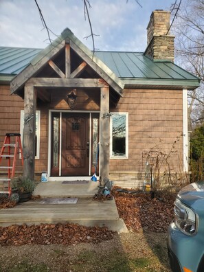 Une maison en bois avec un toit en métal vert, une porte d’entrée dotée de panneaux de verre et une cheminée.