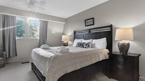 A bedroom with a bed, two bedside lamps, a ceiling fan, a window with curtains, and a framed welcome sign. - Surf Court 30 - Updated 2 Bedroom Condo - Short Walk to Beach (Hilton Head Island)