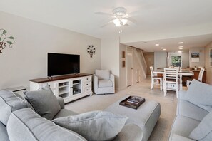 Relax in this spacious living room with a large flat-screen TV, comfortable sofa, and dining area.