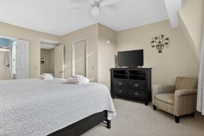 A bedroom with a bed, a television on a dresser, a chair, and a door leading to a bathroom.