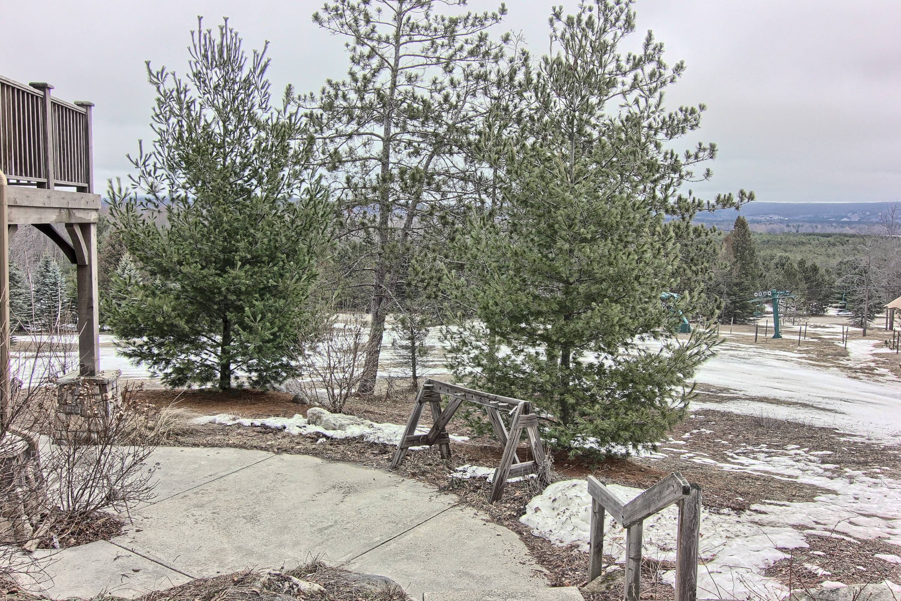 A wooden deck with a swing set, surrounded by snow-covered ground and evergreen trees.