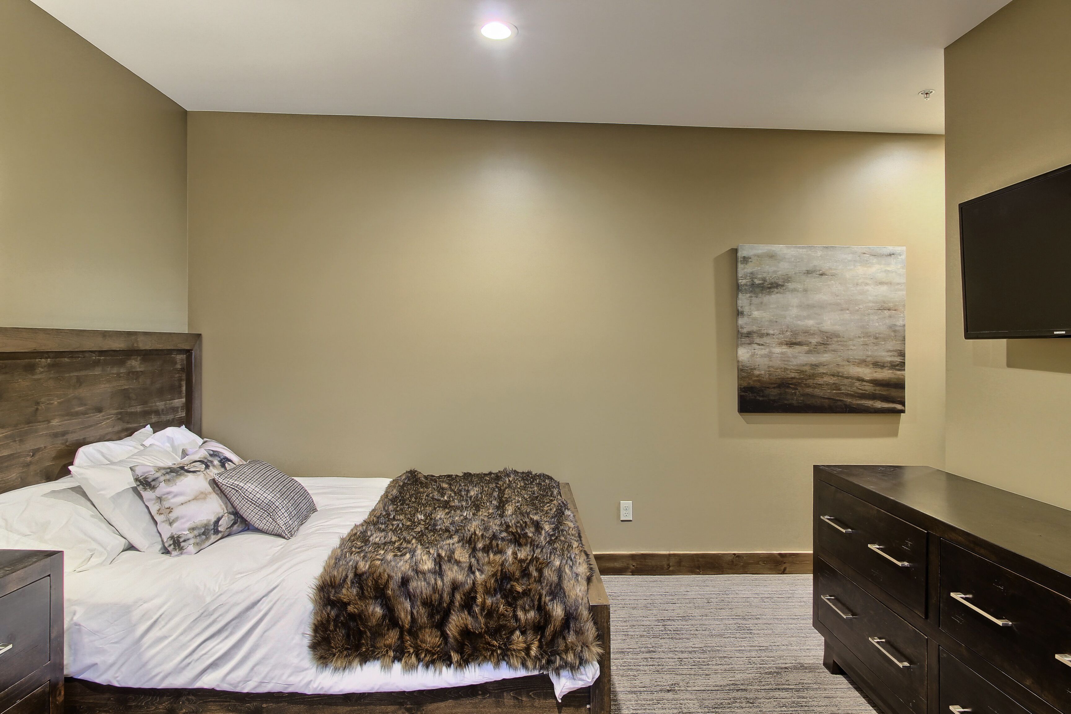 Een slaapkamer met een bed, een dressoir, een schilderij aan de muur en een plafondlamp.