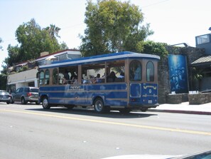 A blue and beige bus with "Laguna Beach Transit" written on the side, parked on a street with cars and buildings in the background.