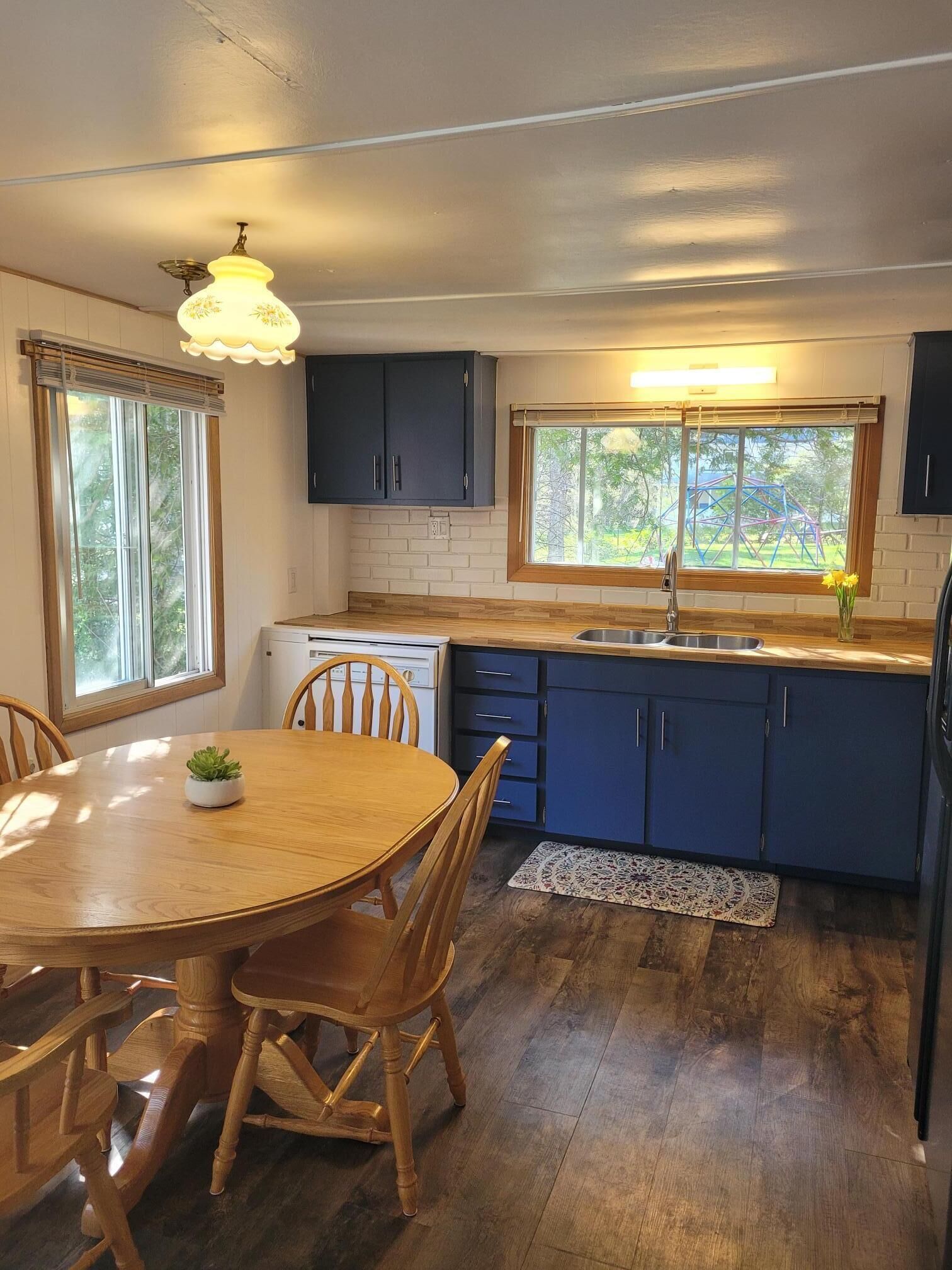 A kitchen with wooden cabinets, a sink, a dining table with chairs, and a window with a view of greenery.