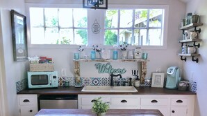 Una cocina con una mesa de madera, armarios blancos, un microondas y una cafetera.
