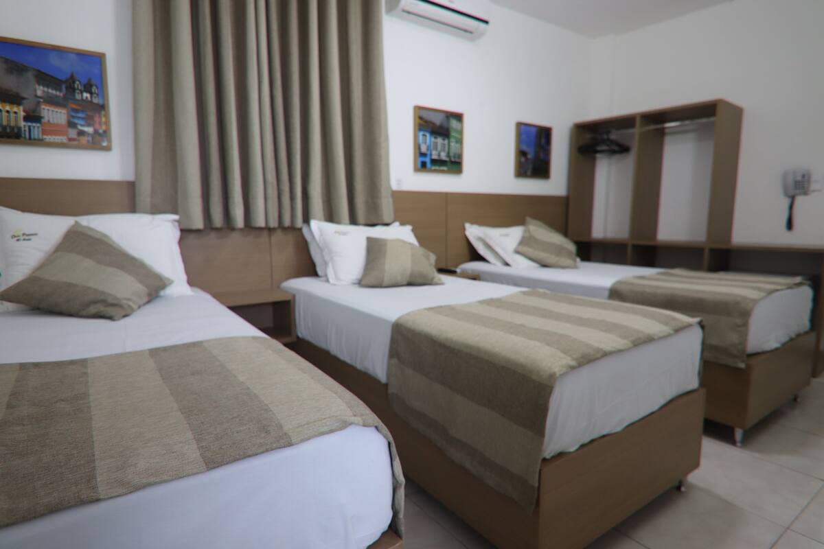 A hotel room with three single beds, a wardrobe, a mirror, and a painting on the wall.