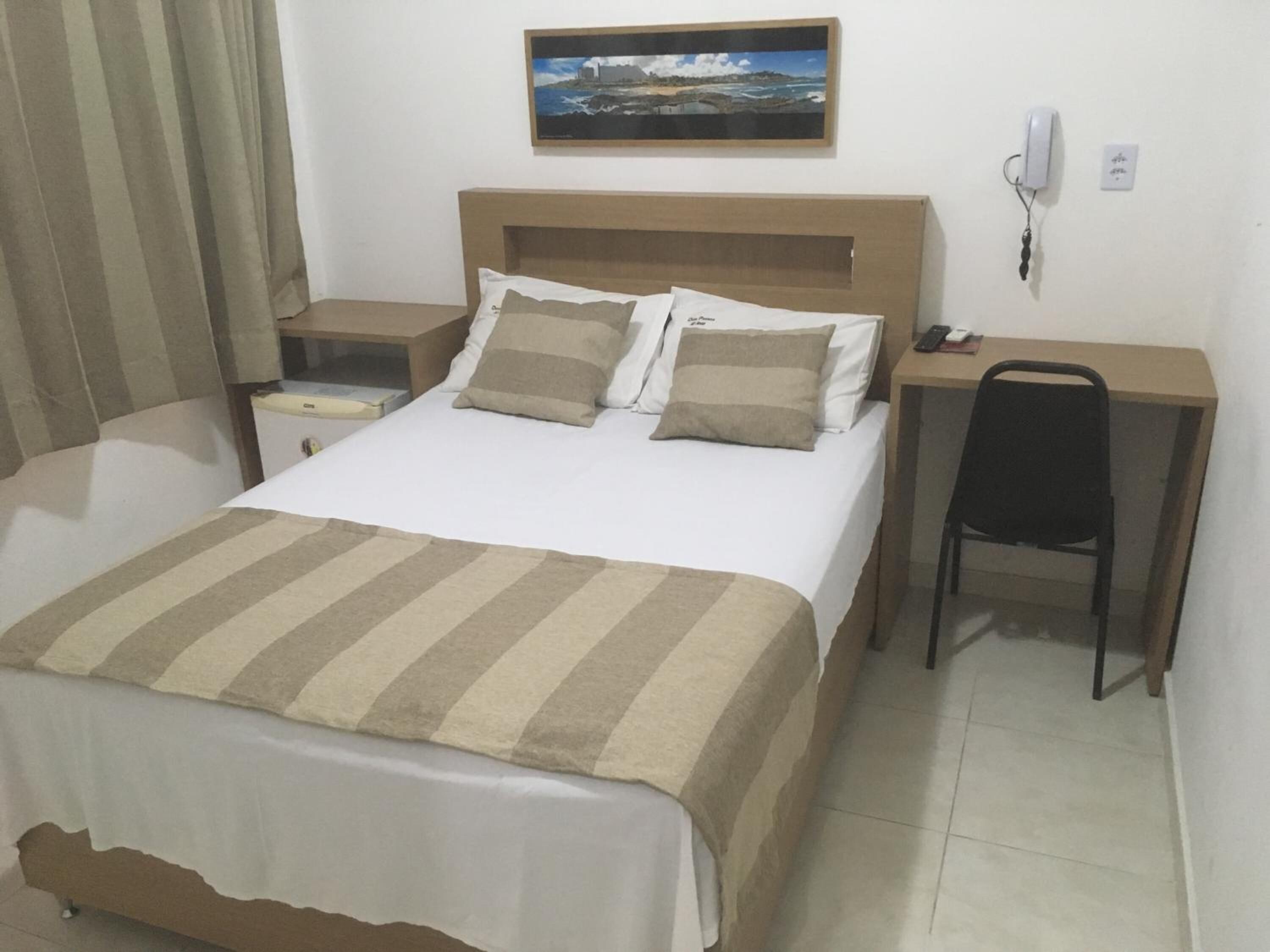 Ein Hotelzimmer mit Bett, Schreibtisch, Stuhl, Nachttisch, Telefon und einem Bild an der Wand.