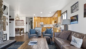 A modern living room with a wooden coffee table, leather sofa, and a dining area with wooden chairs. - Outpost: Sleeping Indian E8 - Hot Tub Access! (Teton Village)