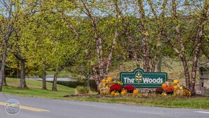 Un letrero que dice 'The Woods' con decoraciones otoñales, incluyendo calabazas y flores.