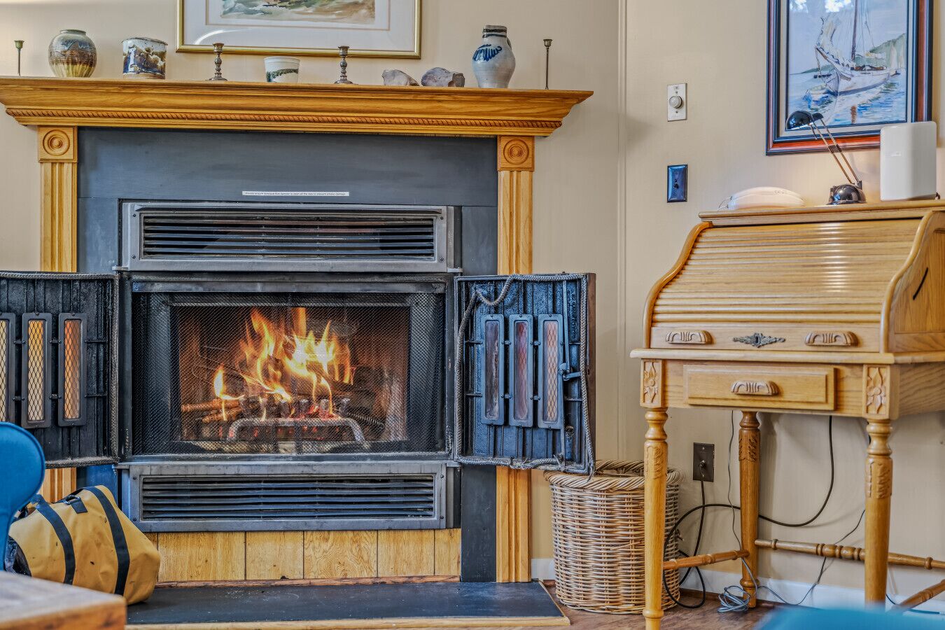 Una chimenea con fuego, una mesa de madera con cajones y una cesta de mimbre en el suelo.