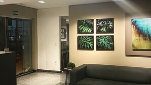 A reception area with a sofa, a glass door entrance, and four framed plant artworks on the wall. - Hotel Alpha (Uberlandia)