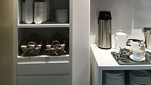 A modern kitchen with white cabinetry, a hanging light fixture, and neatly organized shelves with glassware and kitchenware. - Hotel Alpha (Uberlandia)