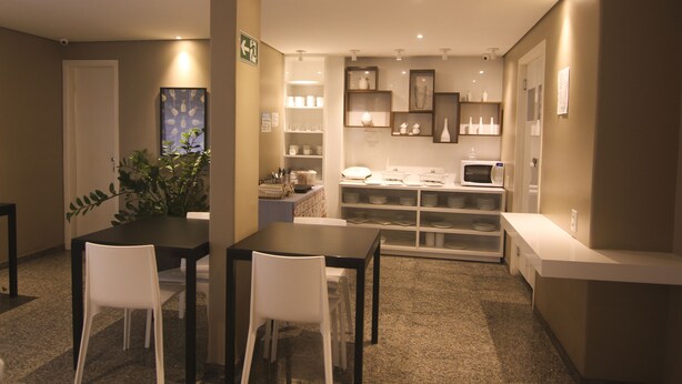 A compact kitchen with white cabinets, a microwave, and a sink. There are two white chairs around a small table, and a potted plant on the left. - Hotel Alpha (Uberlandia)