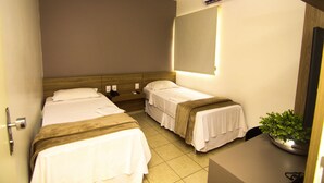 A hotel room with two beds, a bedside table with a plant, a mirror, and an air conditioning unit. - Hotel Alpha (Uberlandia)