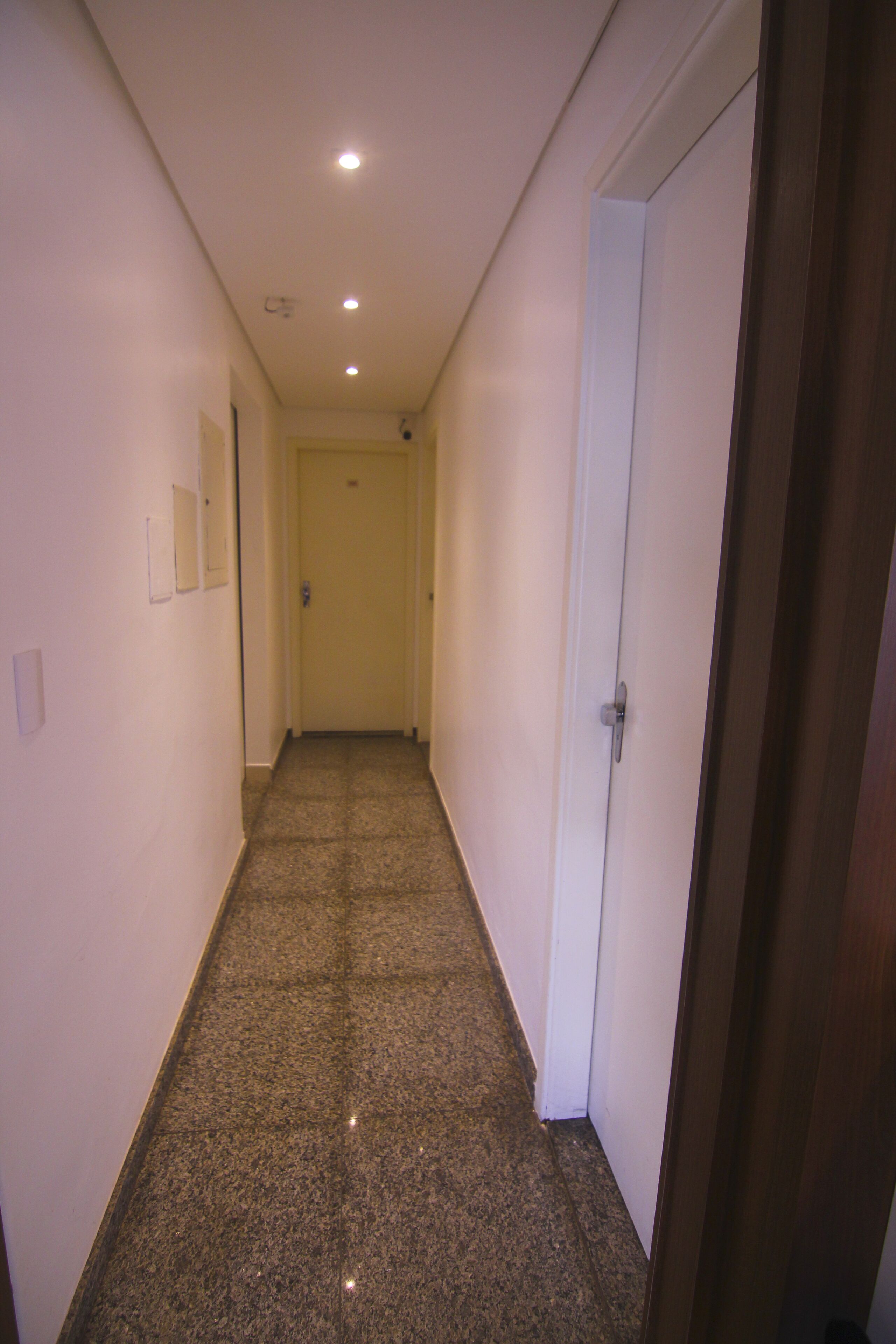 Un pasillo estrecho con una puerta blanca al final, un interruptor de luz en la pared y un suelo con textura.