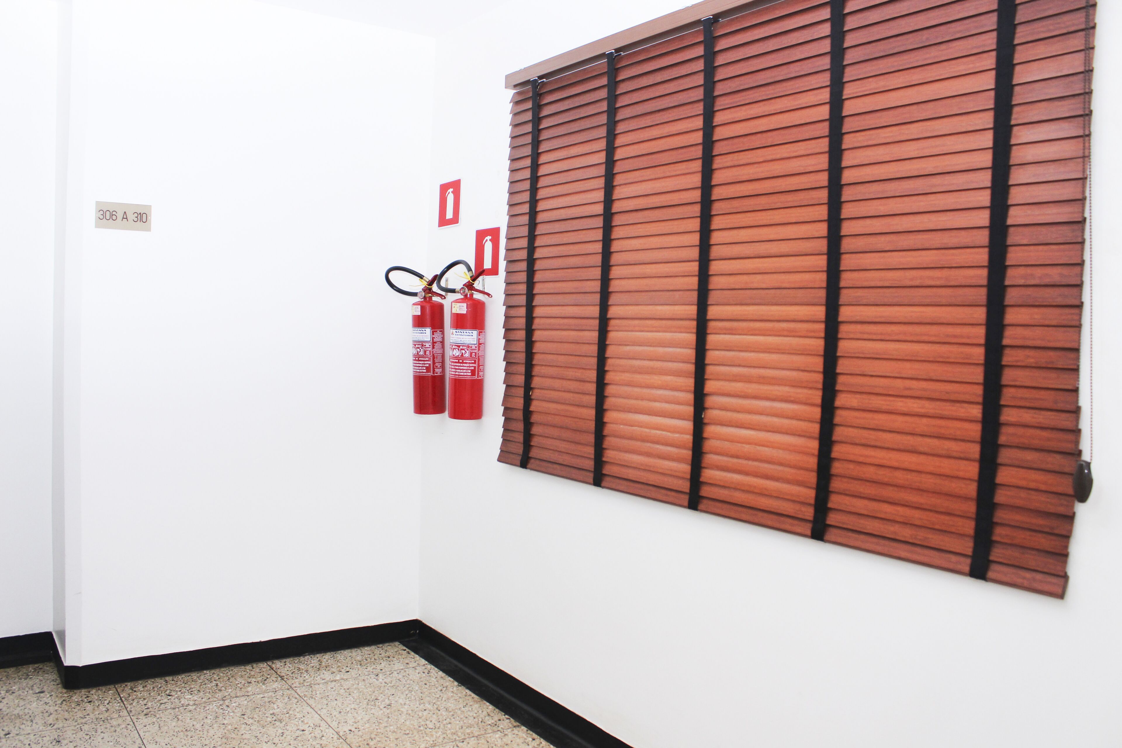 Una habitación con pared blanca, una puerta con un letrero y una ventana con persianas marrones.