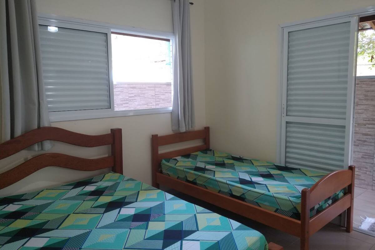 A room with two wooden beds, each with a patterned bedspread. There are two windows with blinds, one of which is partially open.
