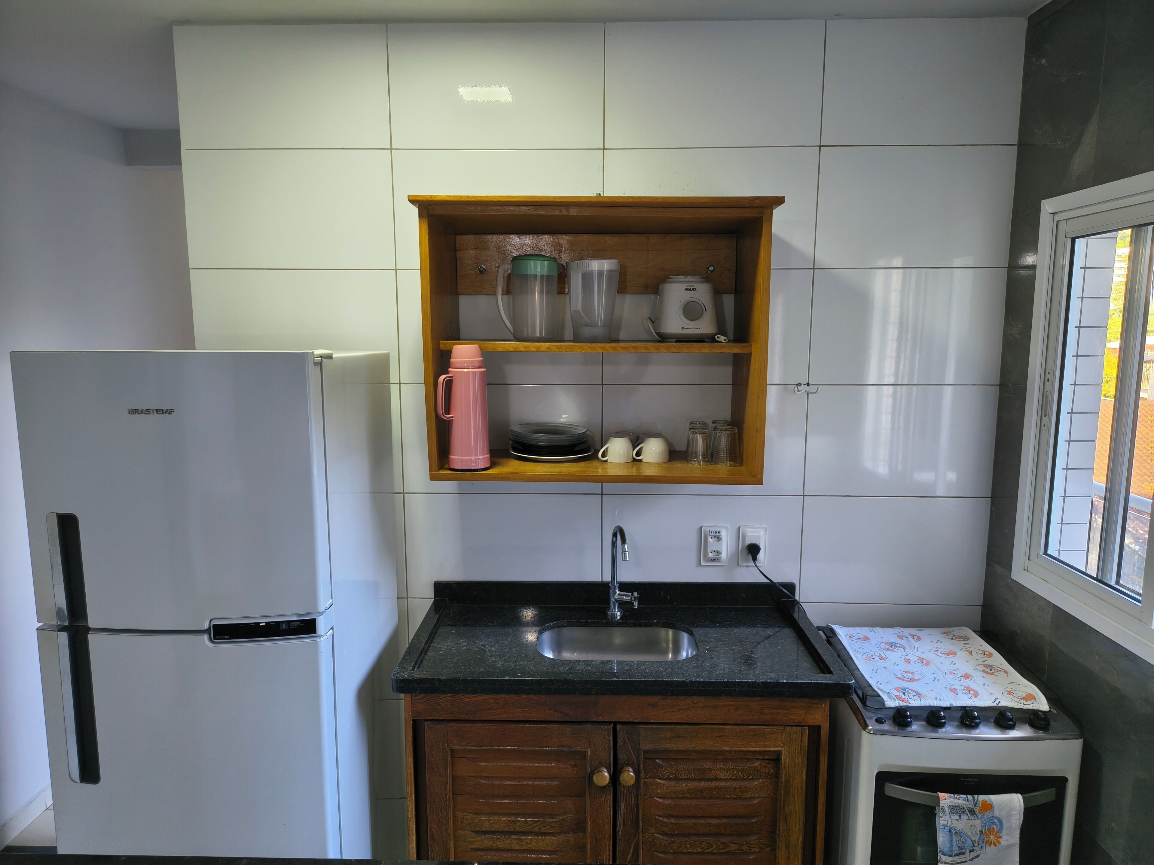 A kitchen with a refrigerator, a sink, a wooden cabinet, and a window.