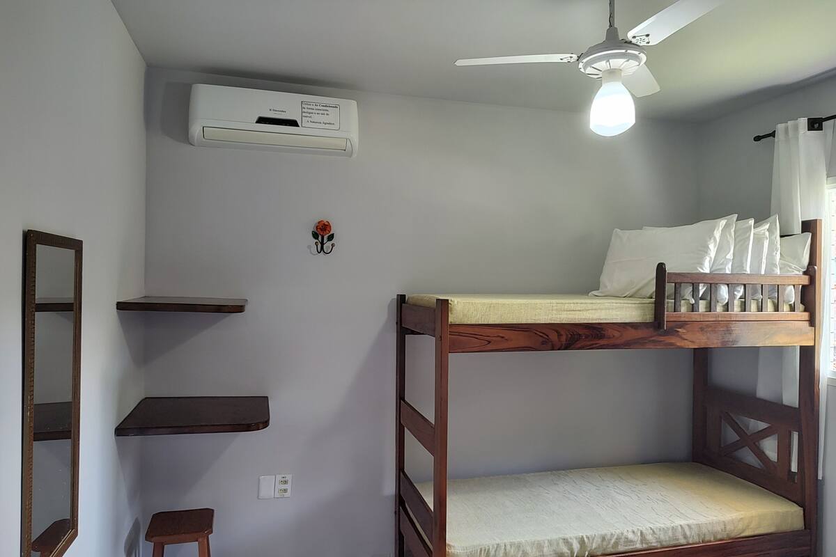 A bunk bed with a wooden frame and a white mattress, a ceiling fan, and a wall-mounted air conditioner.