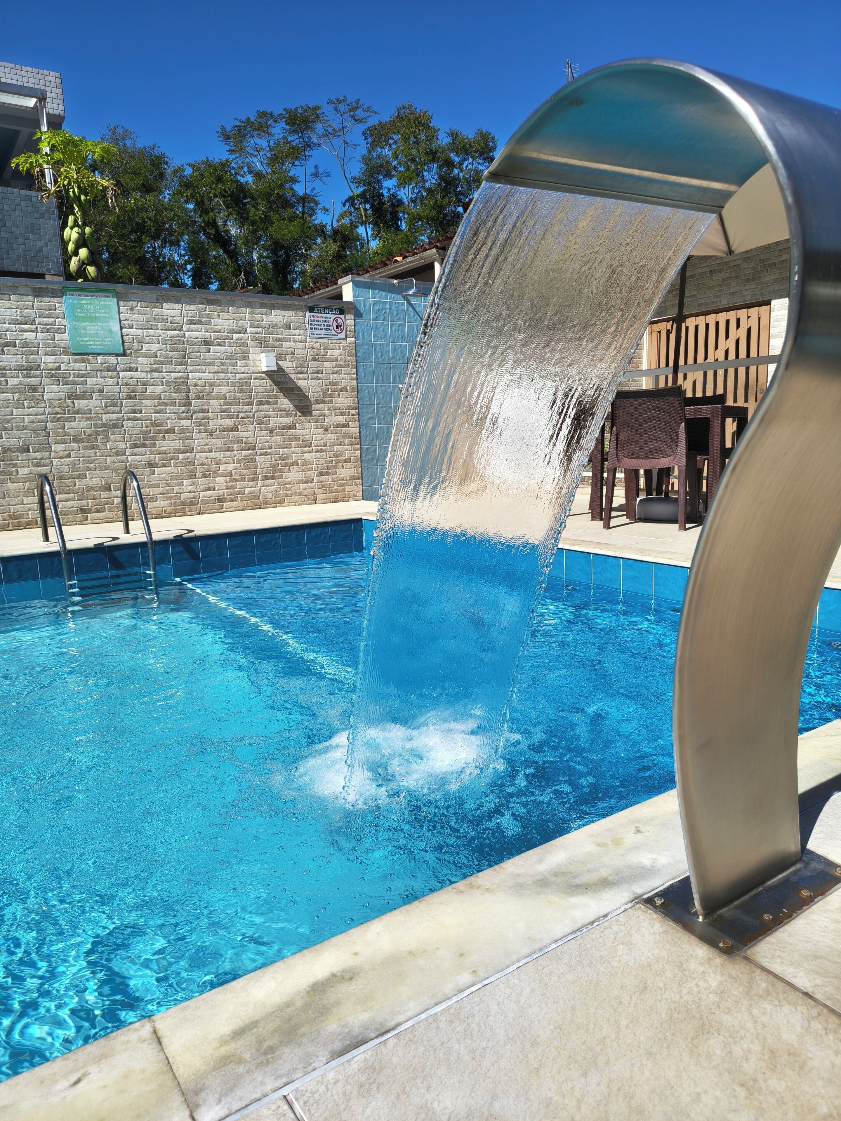 Una piscina con fuente, un muro de piedra y una terraza de madera con sillas.