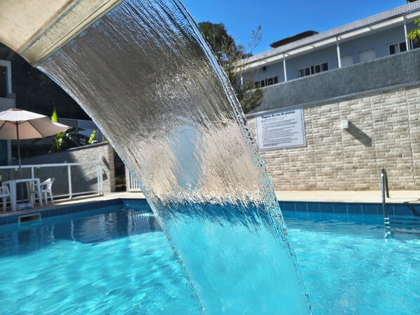 Uma piscina com superfície de água cristalina, barreira de vidro e parede revestida ao fundo.