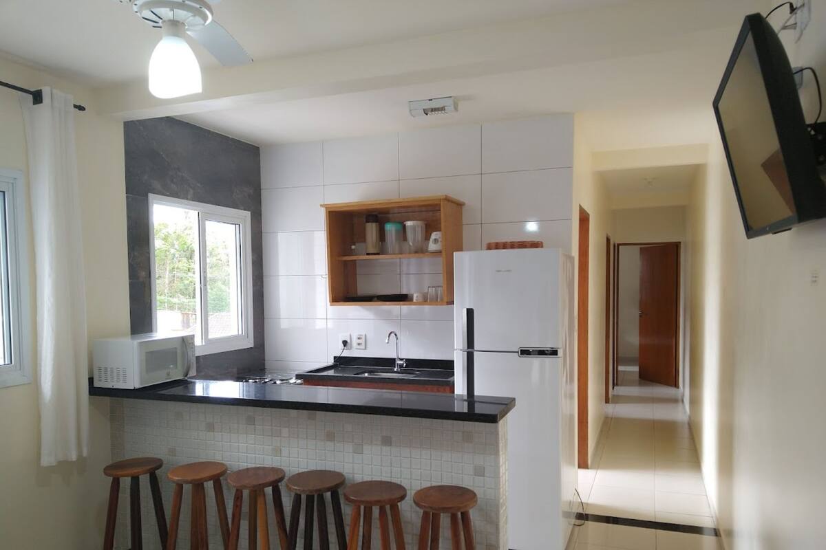 A modern kitchen with a black countertop, white cabinets, a built-in microwave, a refrigerator, and wooden stools.