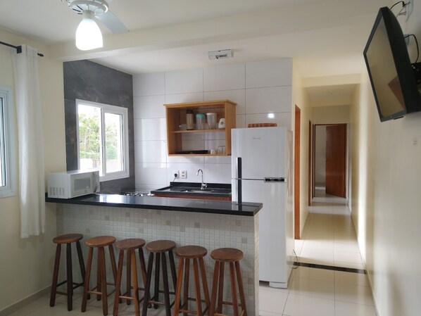 A modern kitchen with a black countertop, white cabinets, a built-in microwave, a refrigerator, and wooden stools.