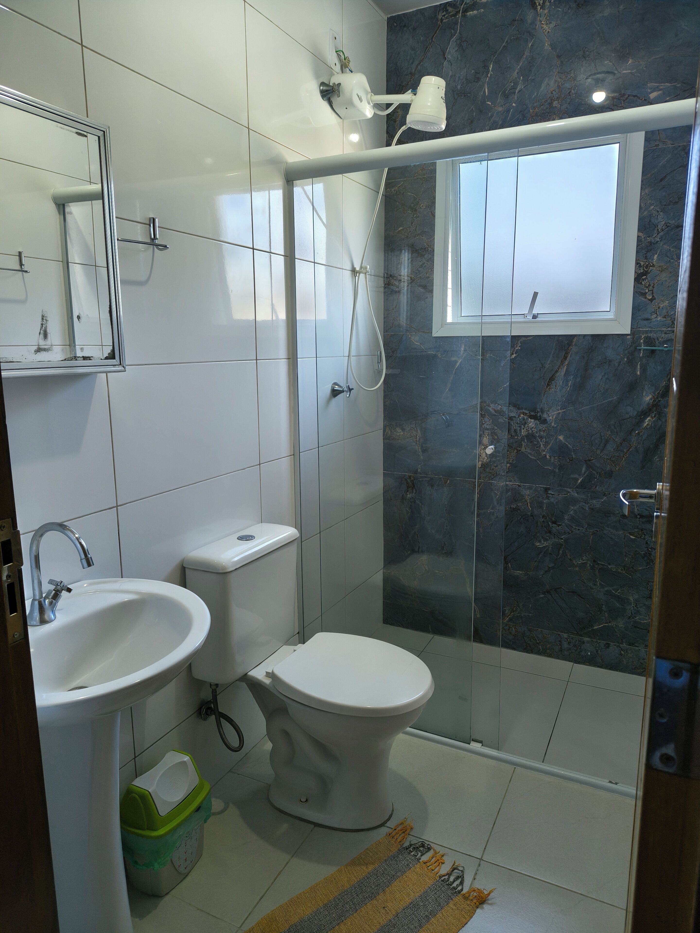 A bathroom with a toilet, sink, and shower area, featuring white tiles and a marble accent wall.