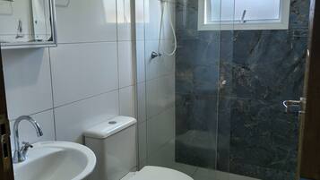 A bathroom with a toilet, sink, and shower area, featuring white tiles and a marble accent wall.