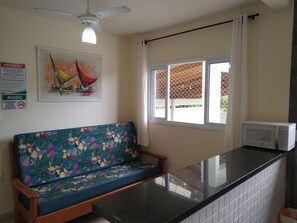 A kitchenette with a microwave, a window with a view, a sofa with a floral pattern, and a ceiling fan.