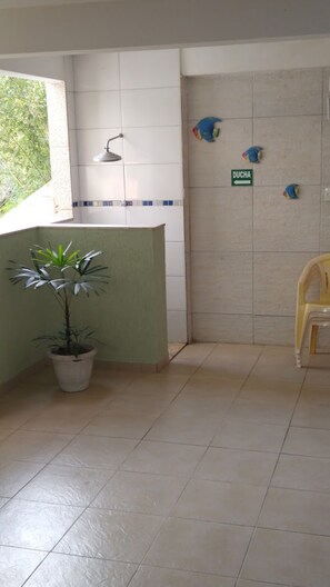 A small, clean room with a potted plant, a shower, and a sign indicating a bathroom. - Canto Verde Apartamentos Caraguá (Caraguatatuba)
