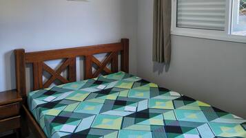 A bedroom with a bed, a ceiling fan, an air conditioning unit, a window with curtains, and a wall-mounted picture.