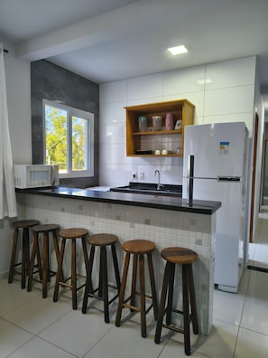 A kitchen with a white refrigerator, a microwave, a sink, and wooden stools.