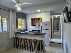 A modern kitchen with a central island, bar stools, a refrigerator, and a ceiling fan.