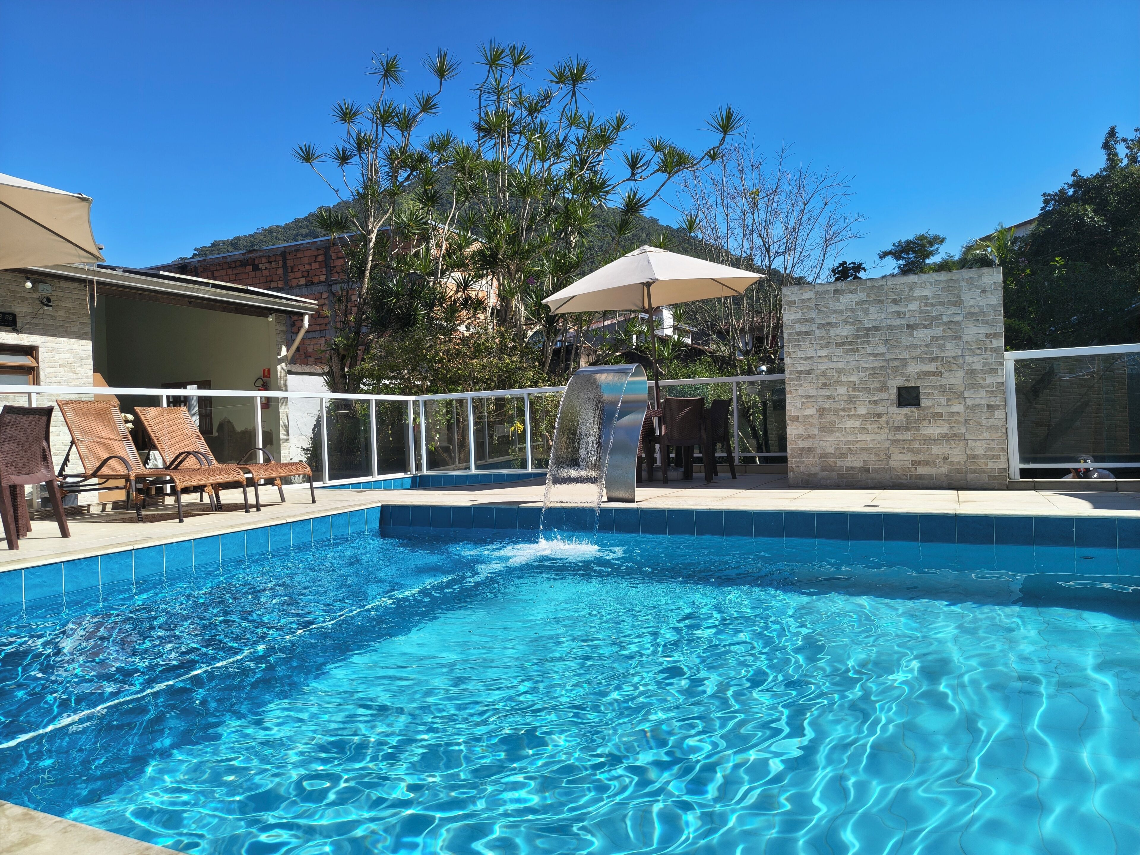 A swimming pool with a waterfall feature, surrounded by lounge chairs and a covered seating area.