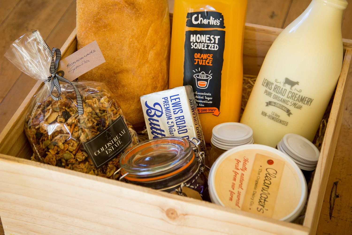 Una caja de madera con varios alimentos, como granola, mantequilla, jugo de naranja y productos lácteos.