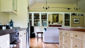 A kitchen with wooden floors, white cabinetry, and a dining area with a table and chairs. - Coldstream Estate - The Whare (Coldstream)