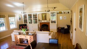 A spacious living room with a fireplace, a wooden dining table, and a bookshelf filled with books. - Coldstream Estate - The Whare (Coldstream)