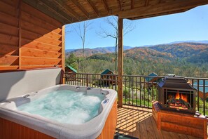 A wooden deck with a hot tub and a fireplace, overlooking a mountainous landscape.