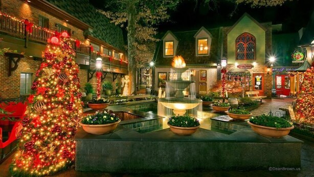 A courtyard with a large Christmas tree, a fountain, and a building with a green facade and a large window. - Moonstruck Apartment 1 (Gatlinburg)