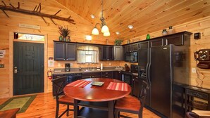 A cozy cabin-style kitchen with dark wooden cabinets, a black refrigerator, and a dining table with chairs. - Moonstruck Apartment 1 (Gatlinburg)