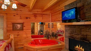 Ein Blockhaus-Interieur mit Holzboden, einer roten Whirlwanne, einem Kamin und einem an der Wand befestigten Fernseher.
