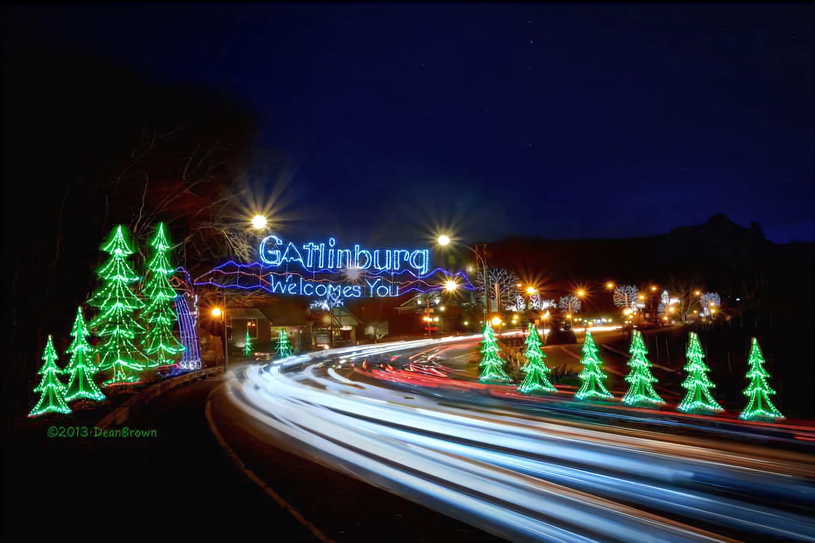 A nighttime view of Gatlinburg with illuminated Christmas trees and a neon sign welcoming visitors.