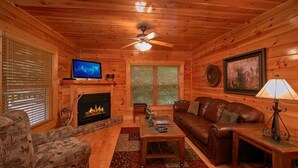 A cozy cabin interior with a fireplace, leather sofa, and a television. - Natural Attractions Apartment 3 (Gatlinburg)