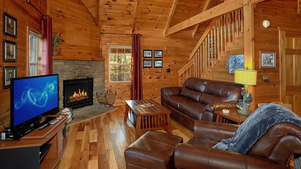 A cozy log cabin interior with a stone fireplace, leather furniture, and wooden beams. - Moonshiners View Apartment 2 (Gatlinburg)