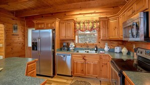 A cabin-style kitchen with wooden cabinets, a stainless steel refrigerator, a dishwasher, a microwave, and a stove. - Moonshiners View Apartment 2 (Gatlinburg)