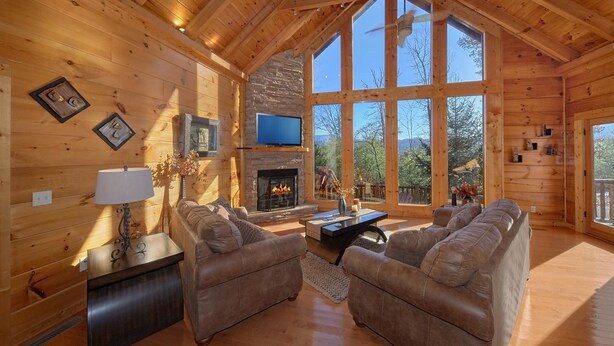 A cozy log cabin interior with a fireplace, comfortable seating, and large windows offering a view of the outdoors. - Tranquility Apartment 2 (Sevierville)