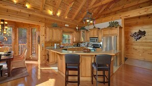 A wooden cabin interior with a kitchen island, bar stools, and a dining area with a table and chairs. - Tranquility Apartment 2 (Sevierville)